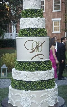 a wedding cake is decorated with grapes and the bride and groom are standing next to it