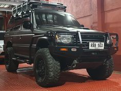 a large black truck parked in front of a building with other vehicles behind it on display