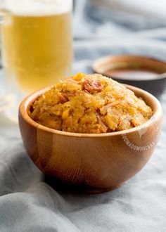 a wooden bowl filled with food next to a glass of beer