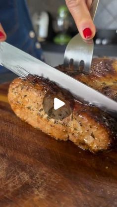 a woman cutting meat with a knife and fork on top of a wooden countertop