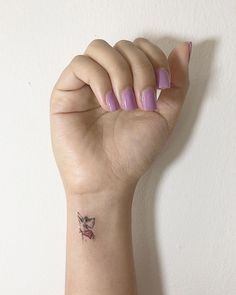 a woman's hand with a small tattoo on her left wrist and purple nail polish