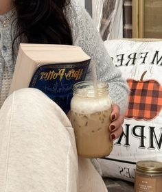 a woman sitting on a couch holding a book and a drink in her right hand