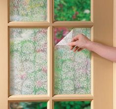 a hand is holding a piece of paper near a window with floral designs on it