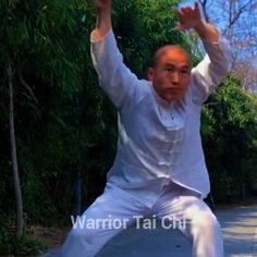 the man is practicing his martial moves on the sidewalk in front of some trees and bushes