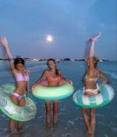 three women in bikinis are on the beach and one is holding an inflatable ring