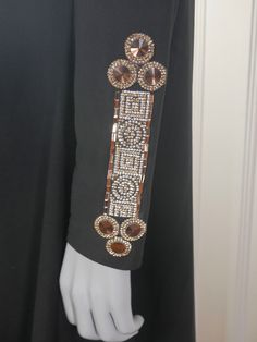 This long black dress has a slight V neckline edged on the left side with glittering diamond crystal and bronze diamanté beads and on the right neckline with larger shimmering bronze rhinestones. The front waistline and sleeve edges also feature such jeweling. The dress has padded shoulders, a loose waistline, and an elegant drop to the floor. The traditional 1980s Syrian abaya dress is unhemed and unlined. A zipper on the left shoulder seam makes dressing an ease. Note that one bronze teardrop Fitted Long Sleeve Embellished Abaya, Rhinestone Abaya Design, Bollywood Style Embellished Long-sleeved Abaya, Gold Embroidered Long Sleeve Abaya, Black Embellished Evening Abaya, Dark Magenta, Jewel Neckline, Abaya Dress, Long Black