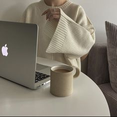 a woman sitting at a table in front of a laptop computer with a sweater over her shoulders