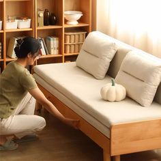 a woman kneeling down next to a bed with white pillows on top of it and a wooden bookcase behind her