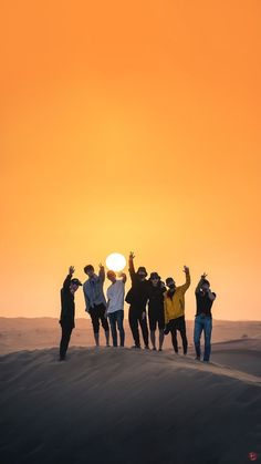 a group of people standing on top of a sand dune under a yellow sky at sunset