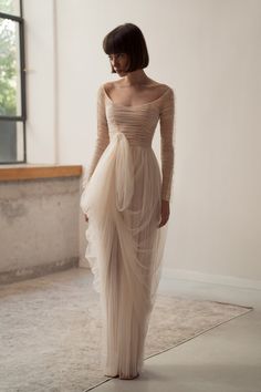 a woman in a long dress is standing near a window