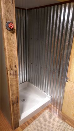 a bathroom with a shower and wooden flooring next to a wall made out of corrugated sheets