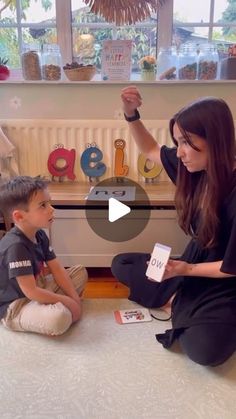 a woman sitting on the floor next to a little boy who is holding a book