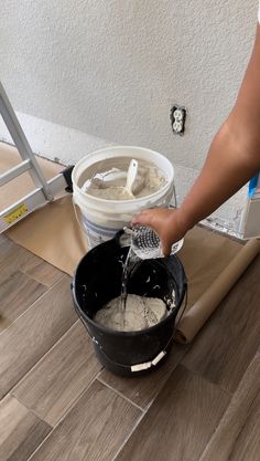 a person pouring cement into a bucket on top of a wooden floor next to a ladder