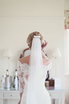 the back of a bride's wedding dress, with her veil pulled back and she is looking at herself in the mirror