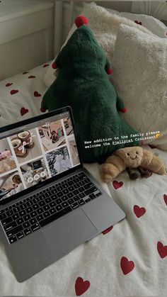 an open laptop computer sitting on top of a bed next to a stuffed animal and pillow