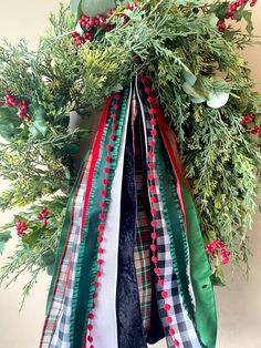 a wreath with green, red and white ribbons hanging from it's centerpiece