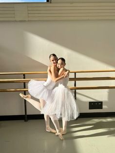 two ballerinas in white tutus posing for the camera with their arms around each other