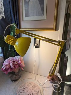 a yellow desk lamp sitting on top of a table next to a vase with flowers