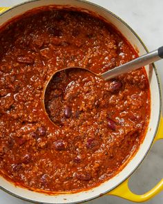 a yellow pot filled with chili on top of a white counter next to a wooden spoon