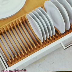 a bunch of white plates are in a wooden tray on the counter top, ready to be put into a dishwasher