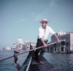 a man on a boat in the water with a long pole and a bird standing next to him