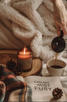 a person pours coffee into a cup next to a book and pine cones on a bed