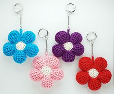 three crocheted flower keychains are shown on a white surface, one is red, one is blue and the other is pink