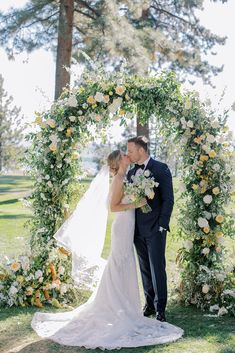 a bride and groom kissing in front of an archway decorated with flowers