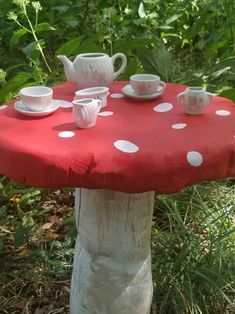 a red table with white polka dots and cups on it in front of green plants