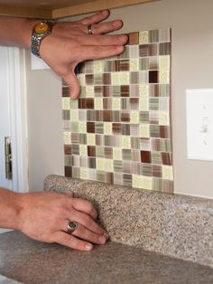 two hands are on the edge of a counter top with a tile wall behind it