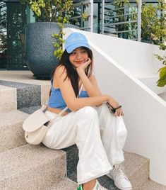 a young woman sitting on the steps with her hand under her chin and wearing a blue hat