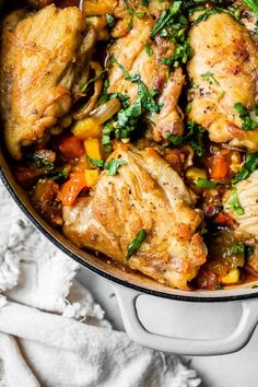 chicken and vegetable stew in a pot on a white surface with a cloth next to it