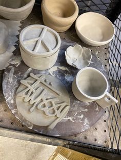 some pottery sitting on top of a metal tray next to cups and spoons with writing written in them