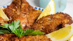 some fried food on a plate with lemon wedges and parsley