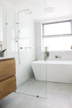 a white bath tub sitting next to a wooden cabinet in a bathroom under a window