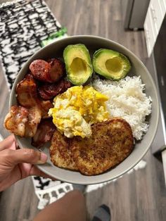 a person holding a plate with eggs, bacon and avocado on it in their hand