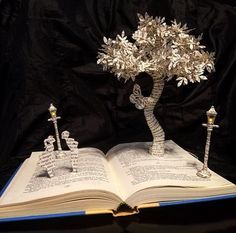 an open book that has some kind of tree on top of it with candles in the middle