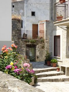 an old stone building with flowers in the foreground and stairs leading up to it