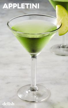 two martini glasses filled with green liquid and an apple slice on the rim, sitting next to each other