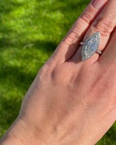 a woman's hand with a diamond ring on top of her finger, and grass in the background