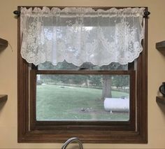 a window with a white curtain and sheep in the grass behind it, next to a kitchen sink