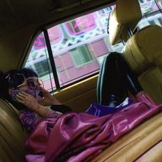 a woman sitting in the back seat of a car talking on her cell phone while holding a purse