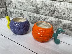 two ceramic mugs sitting next to each other on top of a wooden table in front of a wall