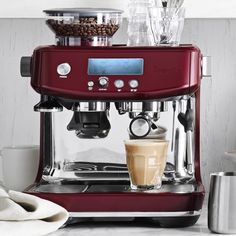 a red espresso machine sitting on top of a counter next to cupcakes