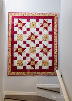 a red and white quilt hanging on the wall next to some stair riser railings