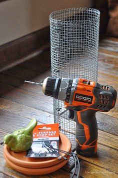 a cordless drill and other tools on a wooden table next to a wire mesh container