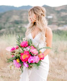 a woman in a white dress holding a pink and yellow bouquet with mountains in the background