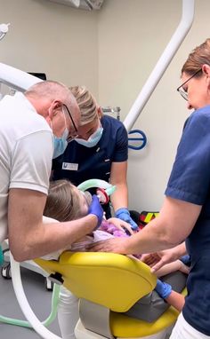 two dentists are examining a child's teeth in the dental chair while an adult looks on