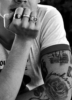 black and white photograph of a man with tattoos on his arms, holding his hand to his mouth