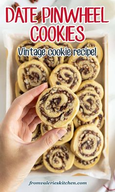 a hand holding a chocolate pinwheel cookie in front of a box full of cookies